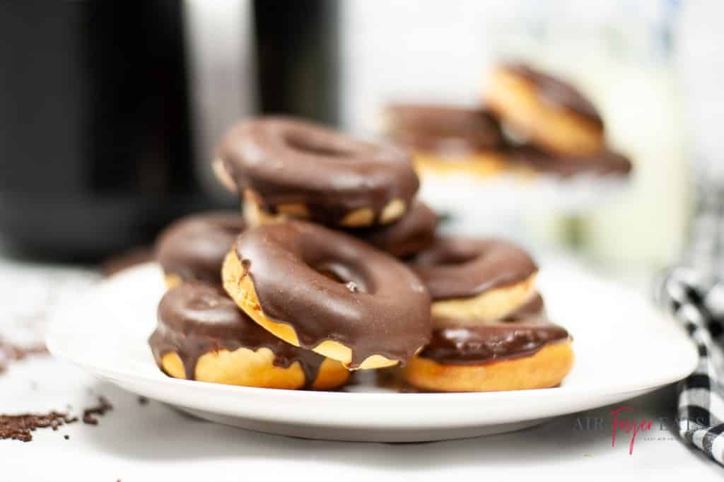 a stack of chocolate glazed donuts on a plate with an air fryer in the background