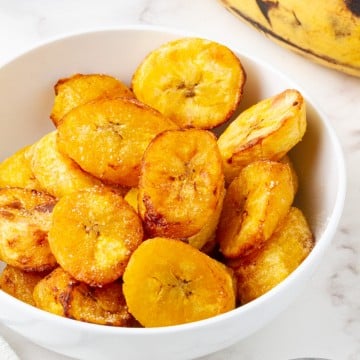 a white bowl filled with cooked plantain slices.