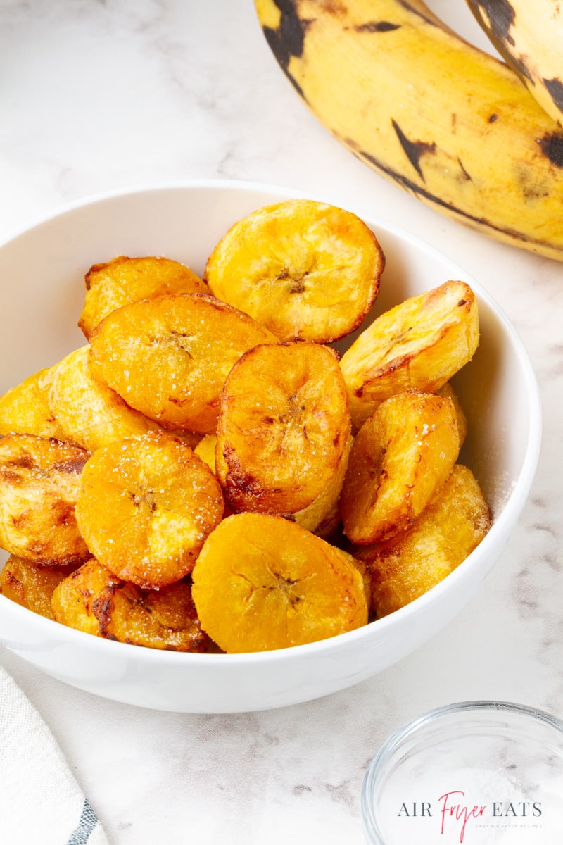 a white bowl filled with cooked plantain slices. 