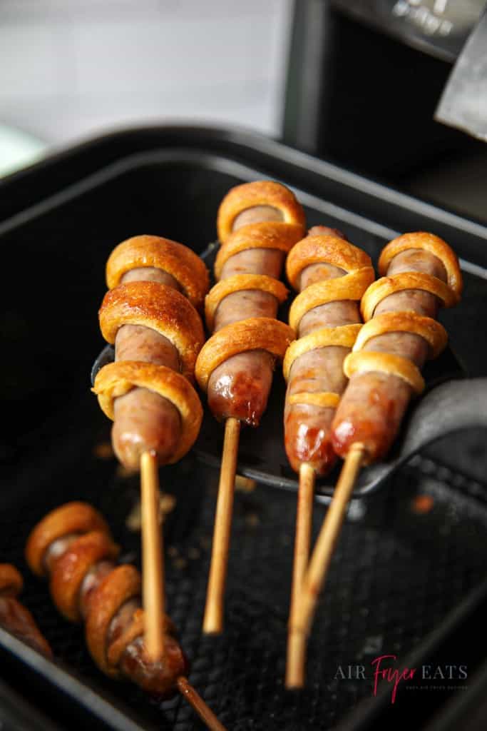 breakfast sausages on a stick wrapped in crescent dough, held over an air fryer basket