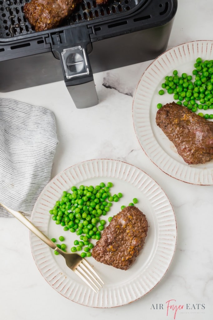 two dinner plates of cube steak and peas next to an air fryer.