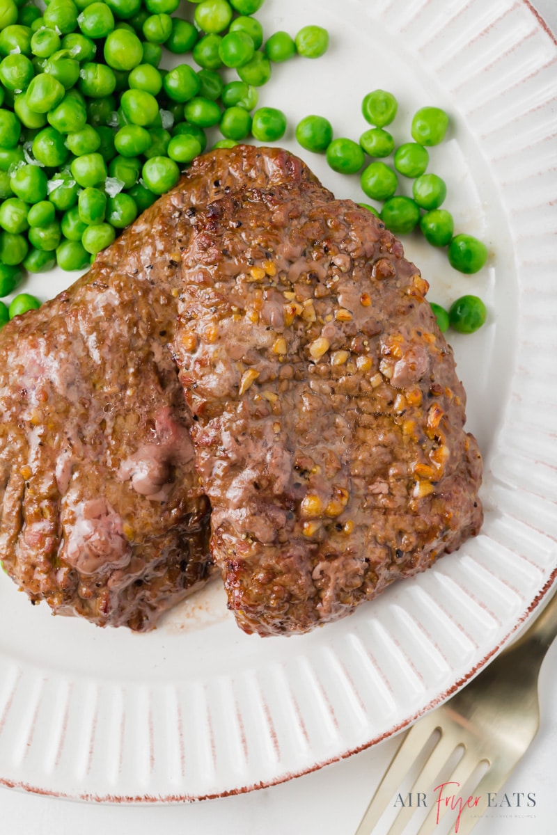 a white scalloped plate with two cube steaks and peas