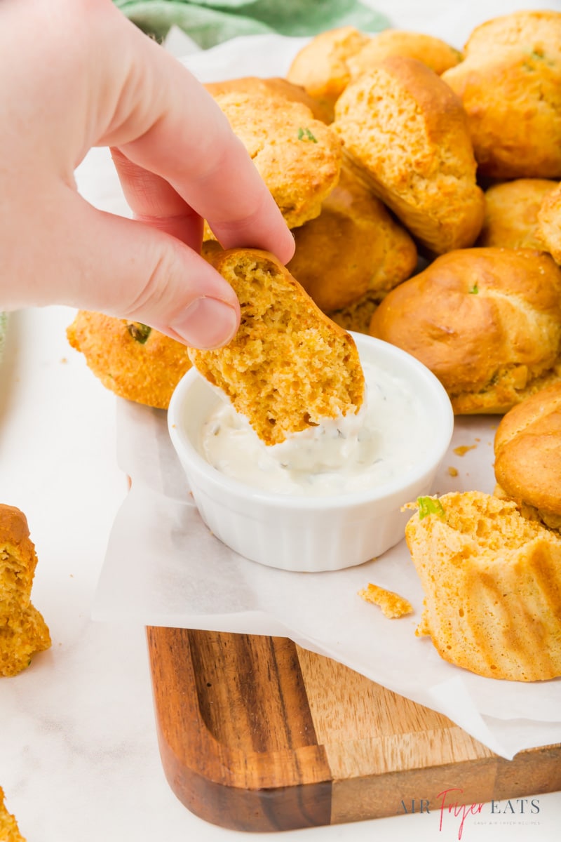 A hand dipping a hush puppy into a creamy white sauce