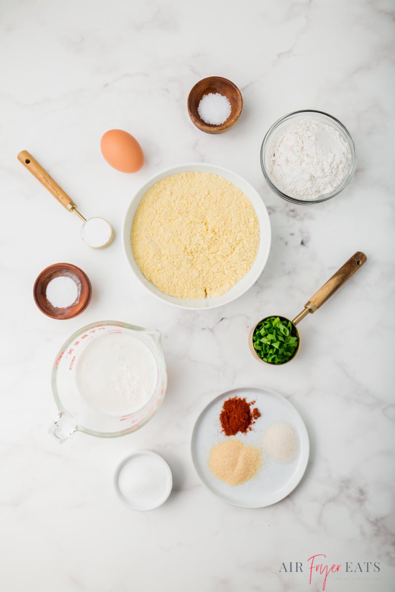 top down shot of all ingredients for air fryer hushpuppies on a marble countertop, each in separate bowls. 