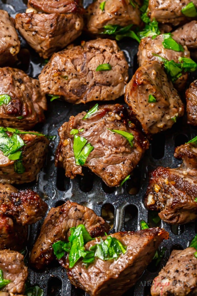 small pieces of steak in an air fryer basket, topped with parlsley