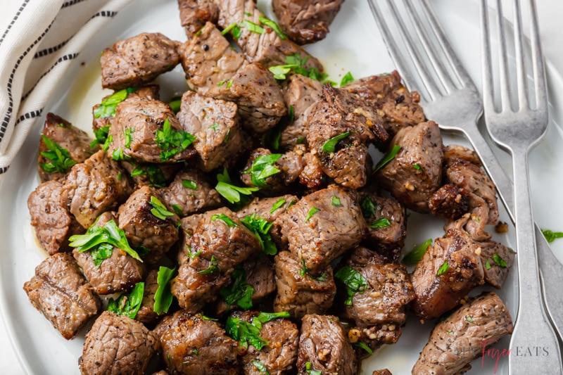 closeup shot of a plate of steak bites topped with parsley,