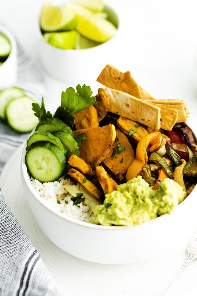 A burrito bowl with sweet potatoes, guacamole, tortilla strips, and rice.