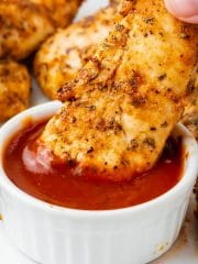 unbreaded air fryer chicken tender being dipped into bbq sauce cup