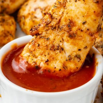unbreaded air fryer chicken tender being dipped into bbq sauce cup