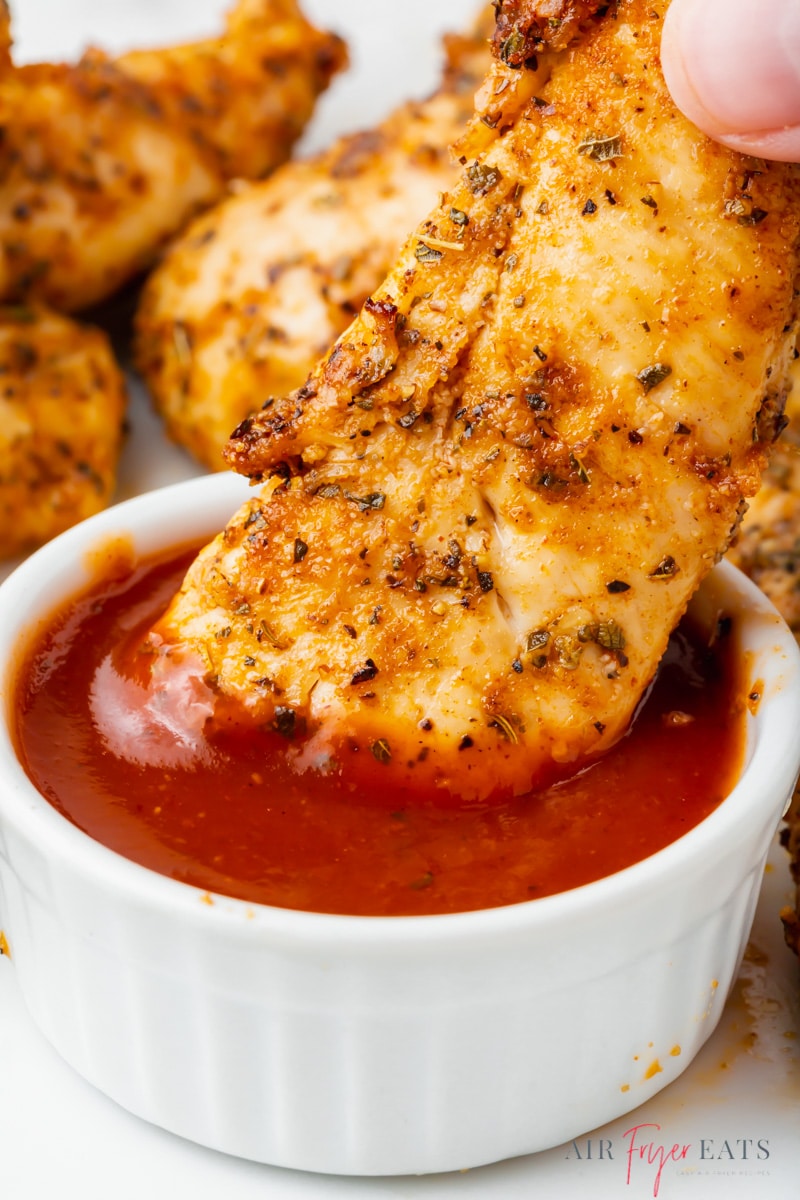 unbreaded air fryer chicken tender being dipped into bbq sauce cup