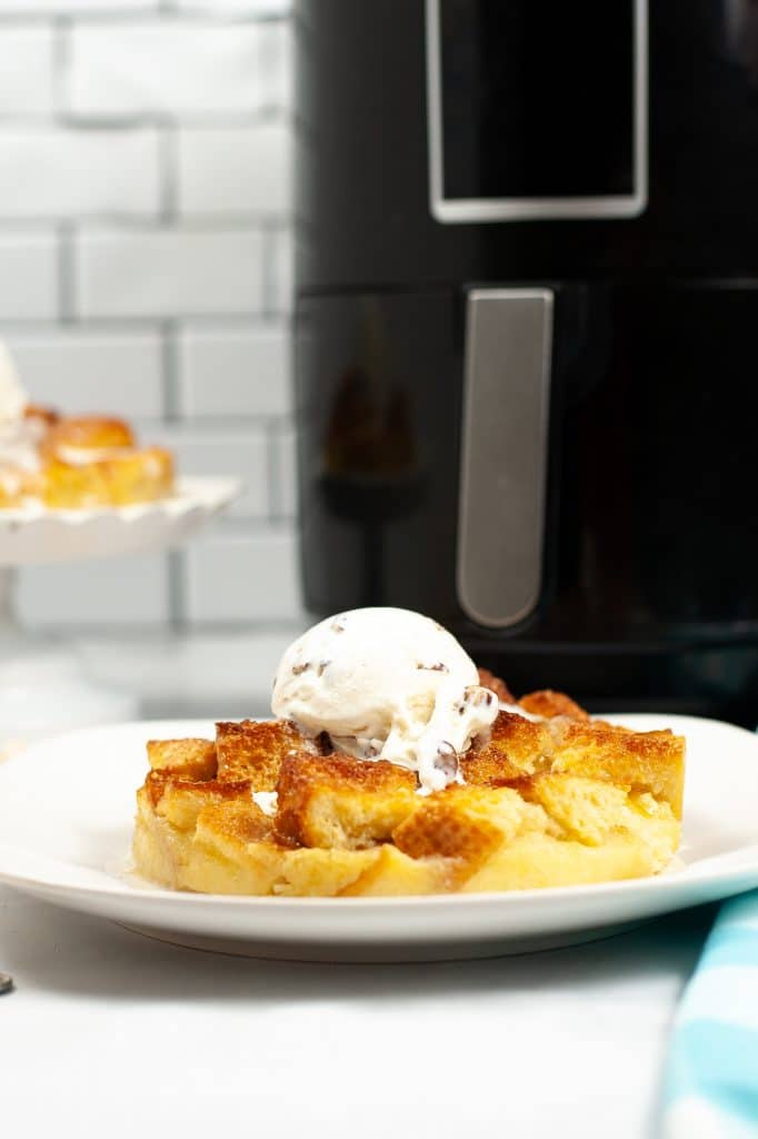 a white plate topped with bread pudding and ice cream, sitting next to an air fryer