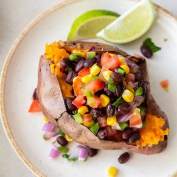 A split sweet potato stuffed with fresh salsa on a plate with two lime wedges
