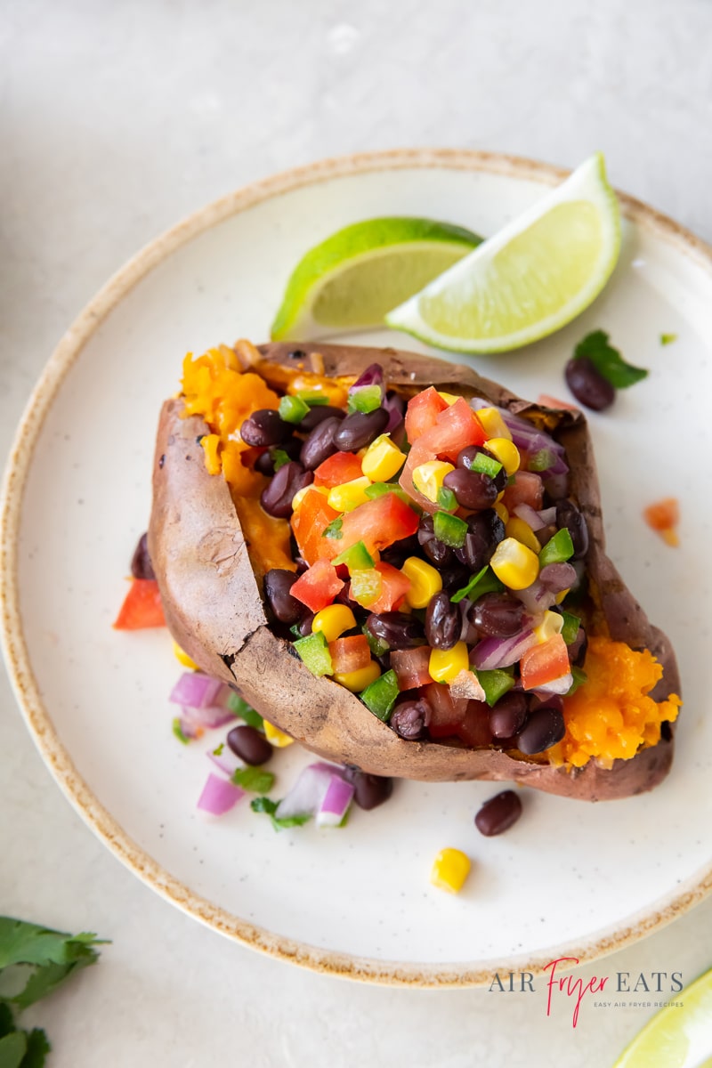 A split sweet potato stuffed with fresh salsa on a plate with two lime wedges