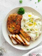 air fryer pork chop with no breading, one whole, another sliced thinly, with a side of mashed potatoes and a parsley sprig