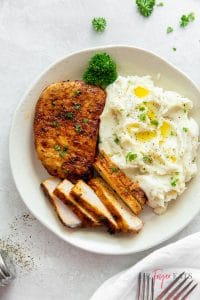 air fryer pork chop with no breading, one whole, another sliced thinly, with a side of mashed potatoes and a parsley sprig