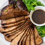 sliced roast beef fanned out on a plate with a cup of au jus and green lettuce garnish
