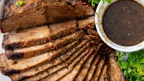 sliced roast beef fanned out on a plate with a cup of au jus and green lettuce garnish