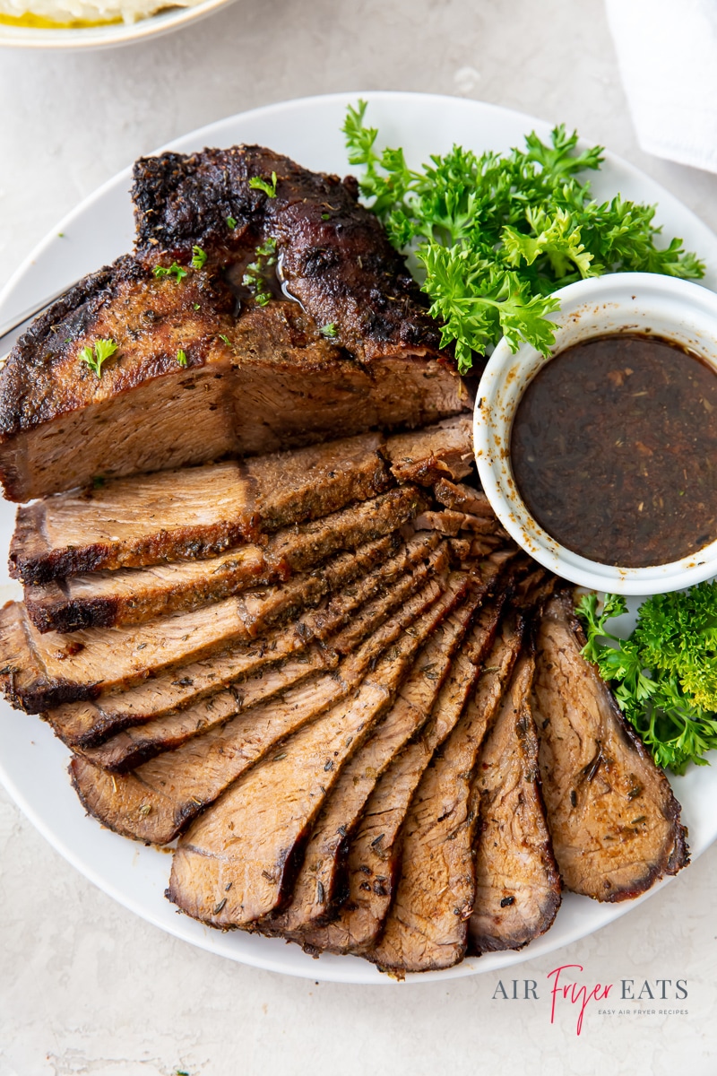 sliced roast beef fanned out on a plate with a cup of au jus and green lettuce garnish