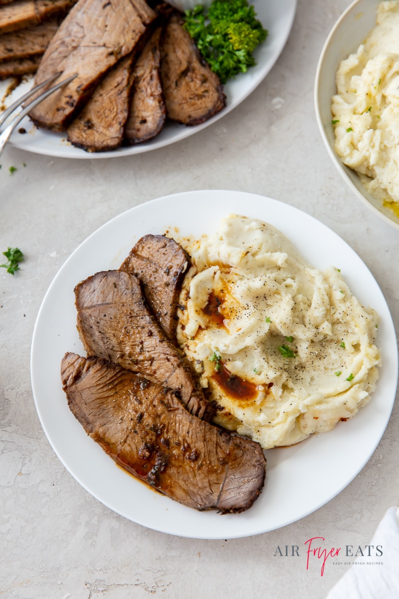 a white plate with sliced roast beef and mashed potatoes