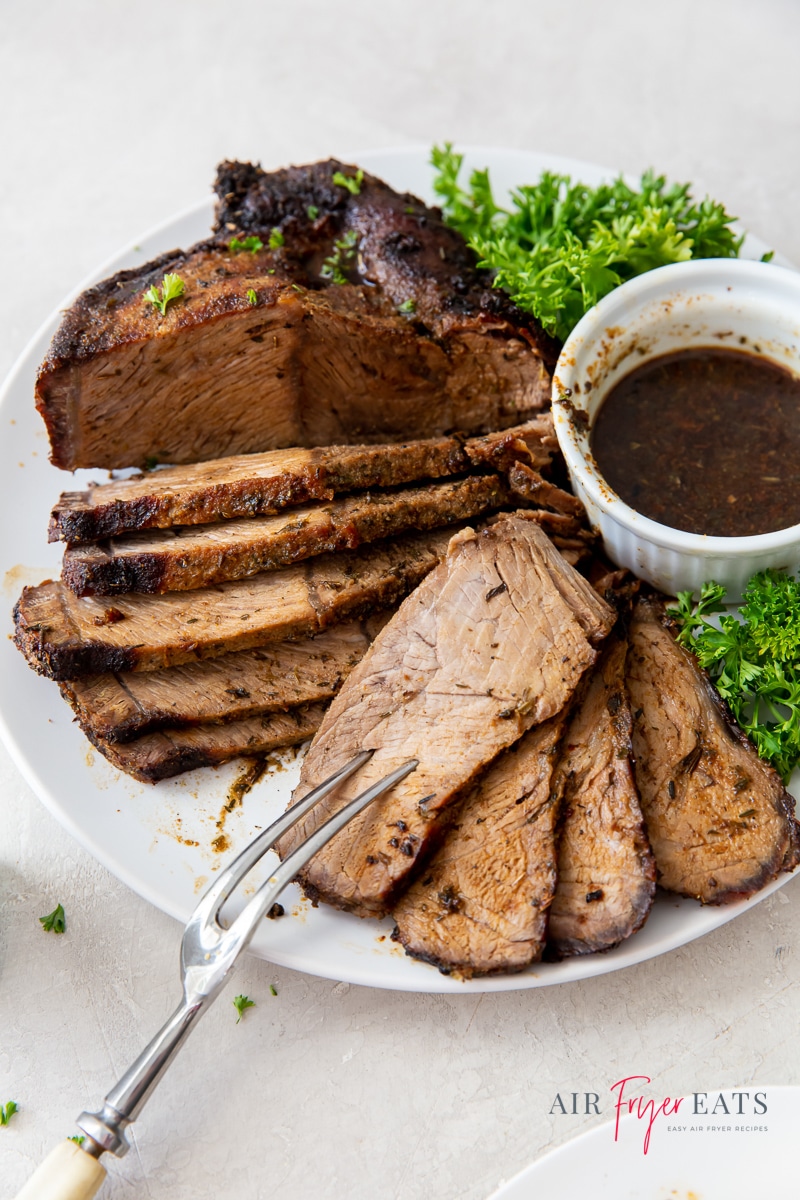 sliced roast beef on a white plate with a cup of au jus