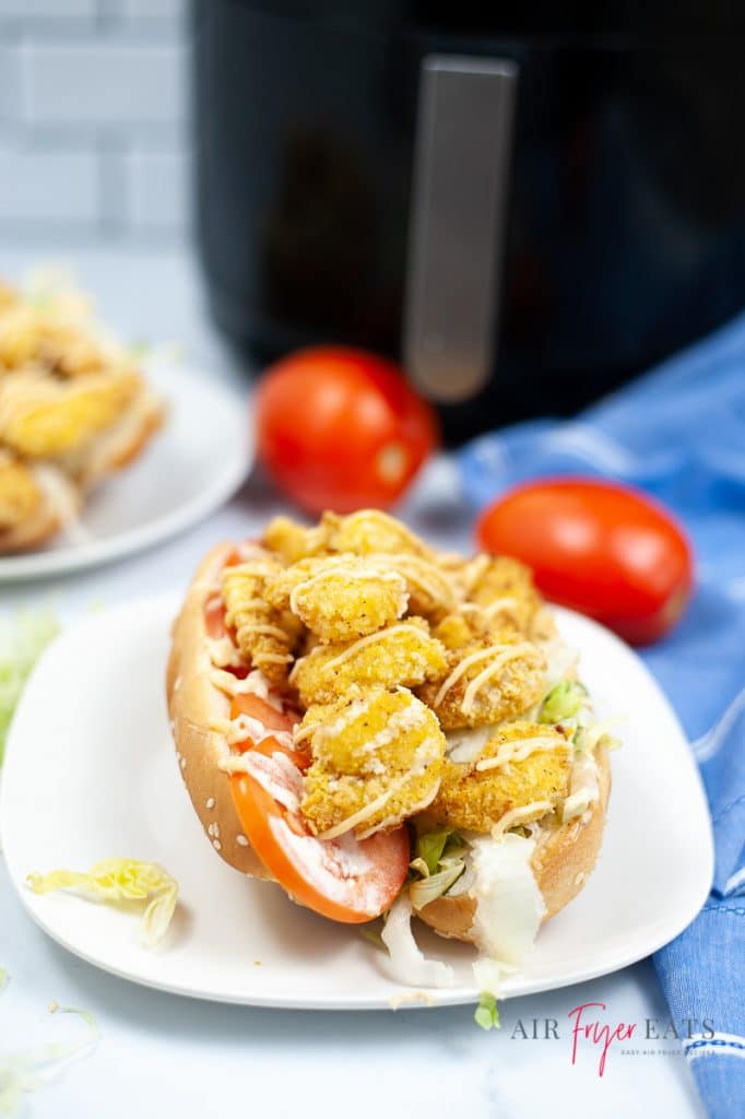 air fryer crispy shrimp po boy on a white plate, garnished with mayo, with a black air fryer in the background