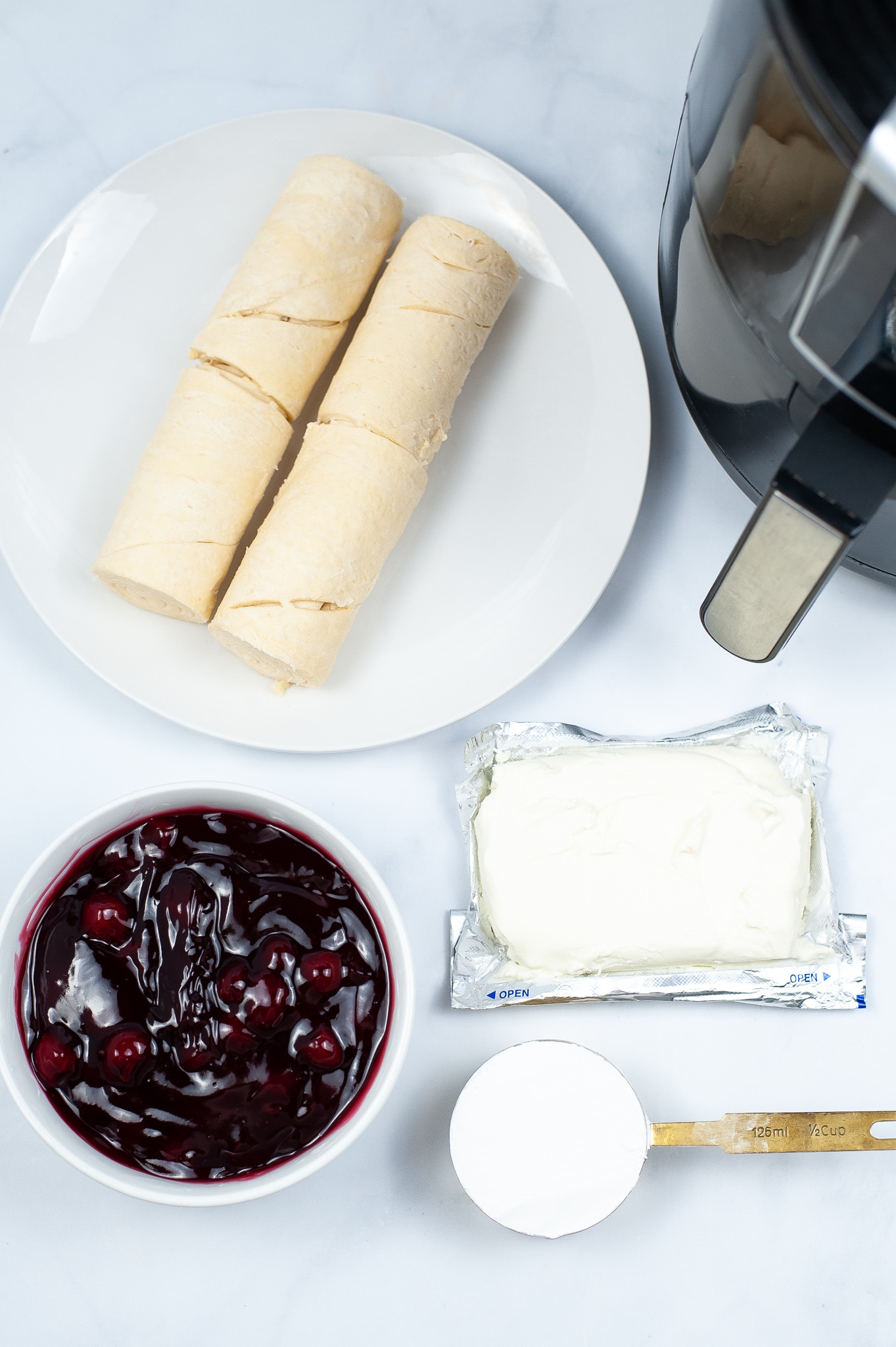 Ingredients for air fryer cherry cream cheese danish, on a countertop, next to an air fryer