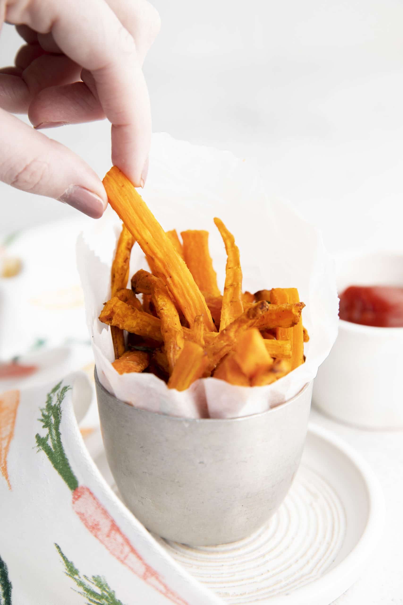 a hand picking up a carrot fry out of a cup full of air fryer carrot fries