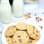 a plate of chocolate chip cookies in front of two glass bottles of milk