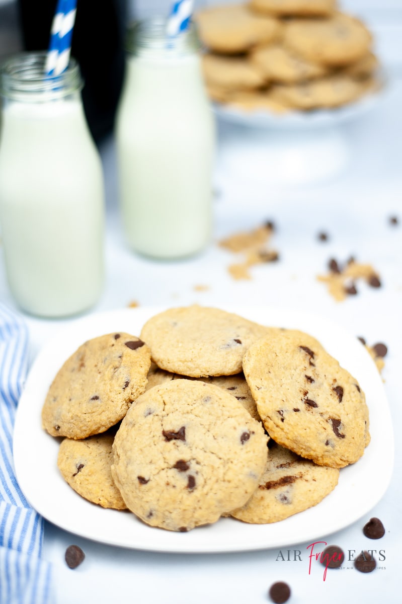 a plate of chocolate chip cookies in front of two glass bottles of milk