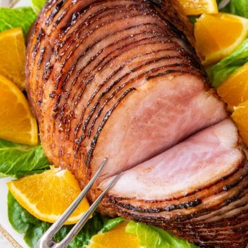 a sliced ham on a platter surrounded by orange slices and green lettuce.