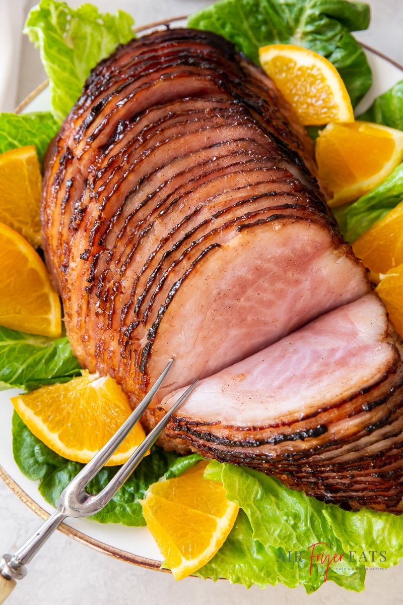 a sliced ham on a platter surrounded by orange slices and green lettuce.