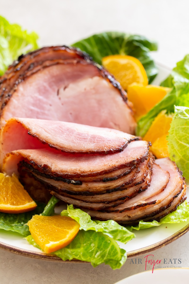 a sliced ham with golden glaze on a bed of green lettuce and orange slices