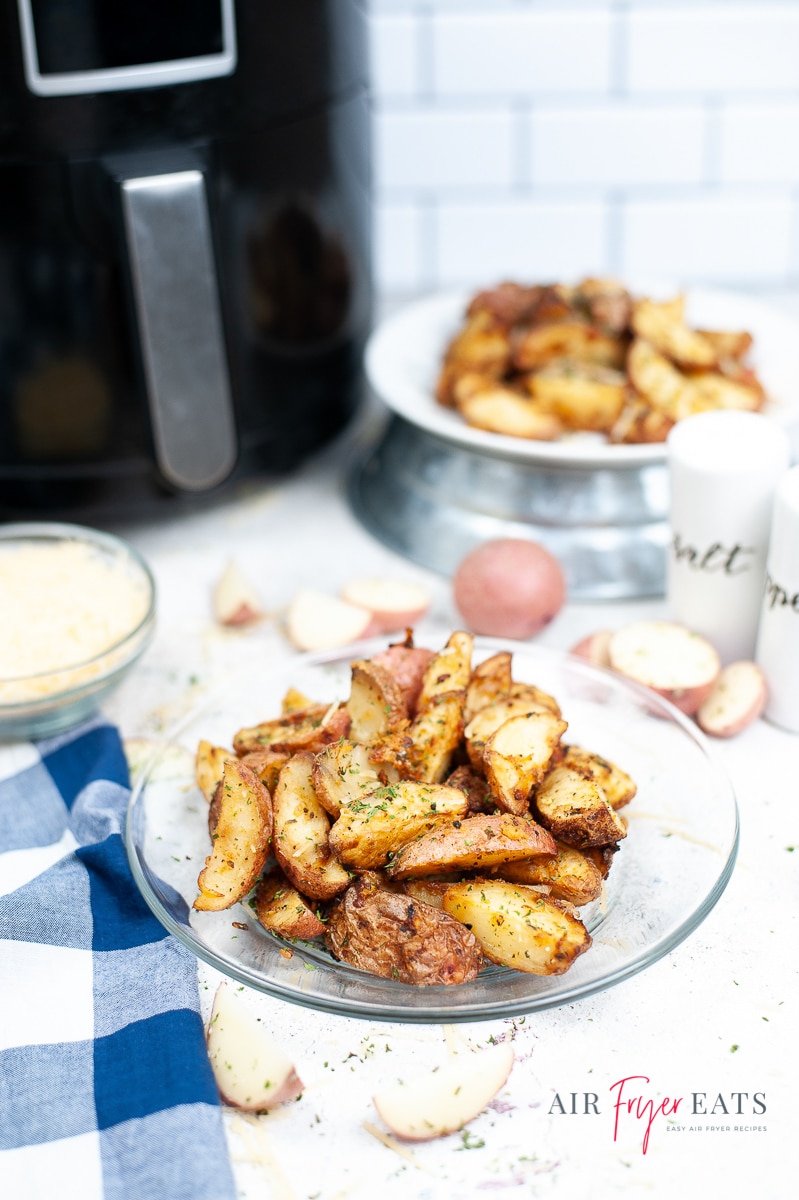 Vertical photo of roast potatoes on a plate. Black air fryer with silver handle in the background.