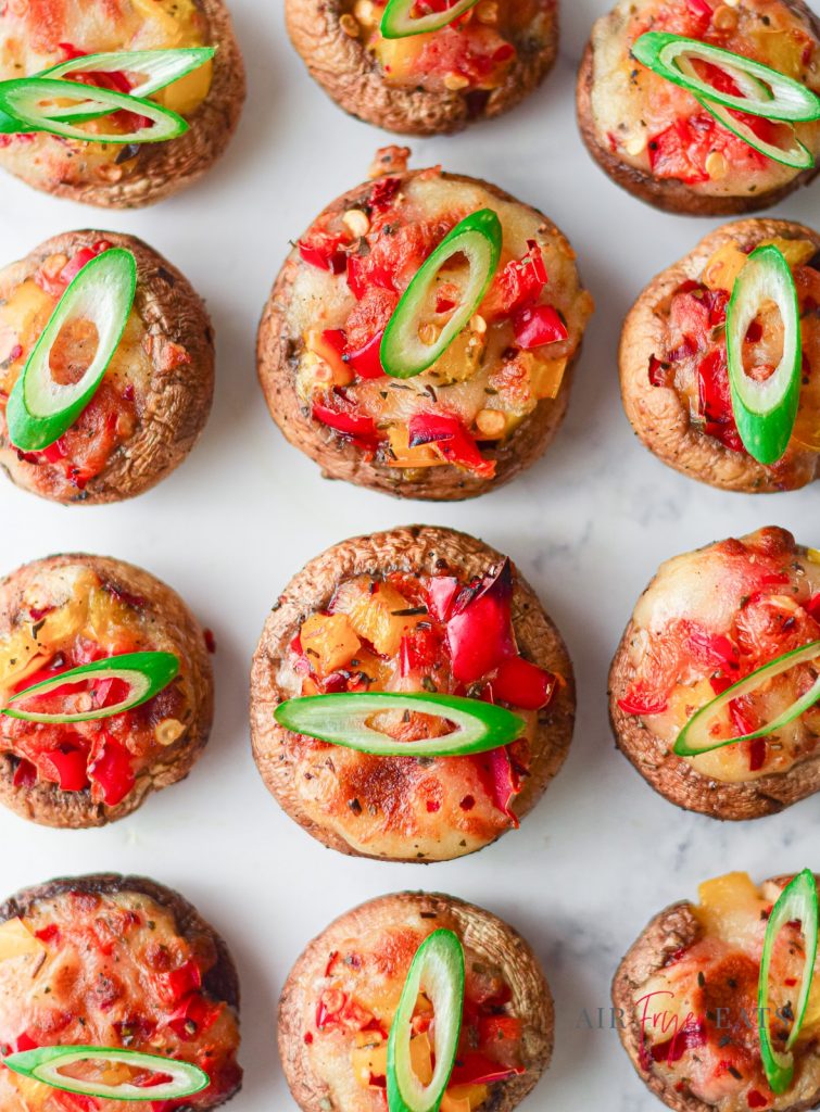 overhead view of stuffed mushrooms with diced tomatoes and green sliced pepper on tops