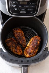 three cooked air fryer chicken breasts in a black air fryer basket