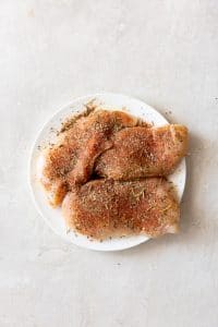 raw chicken breasts with spices on a white plate