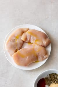 three chicken breasts on a white plate rubbed with oil