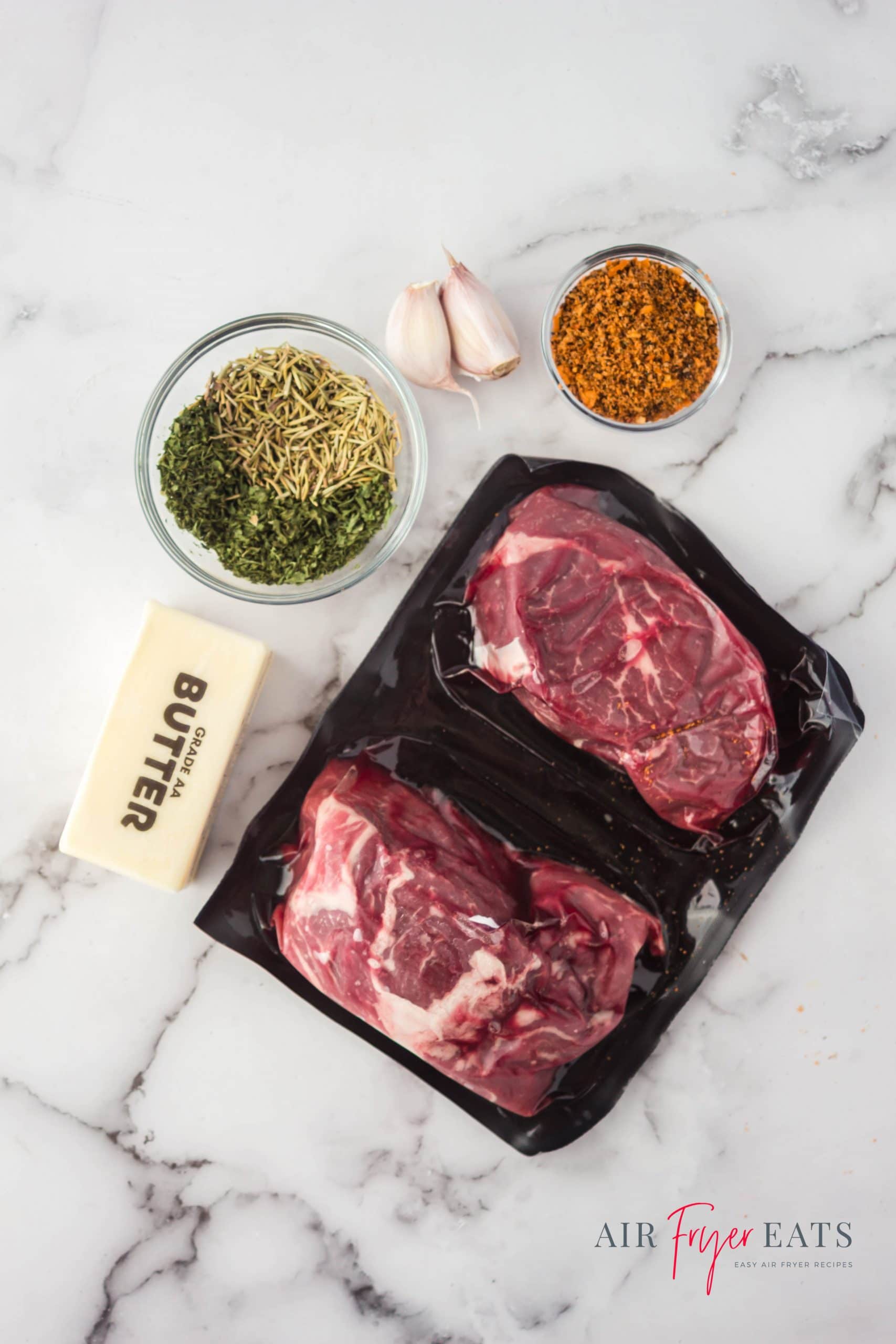 Ingredients for making air fryer steak in the ninja foodi, including herbs, garlic, butter, and thick cut steaks