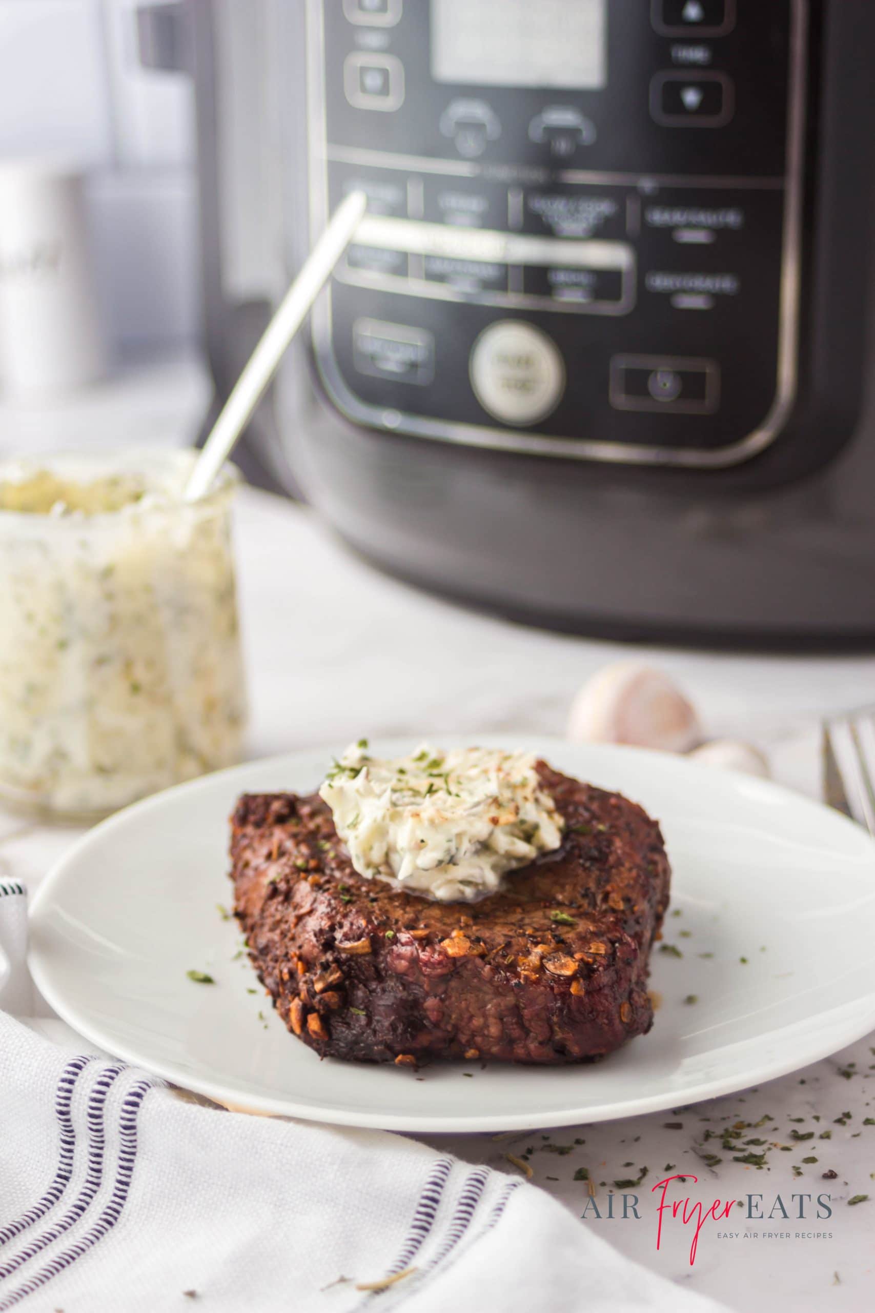 a thick fillet on a white plate topped with compound butter, in front of a ninja foodi