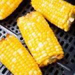Air fryer corn on the cob. Yellow ears of corn sit inside an air fryer basket.