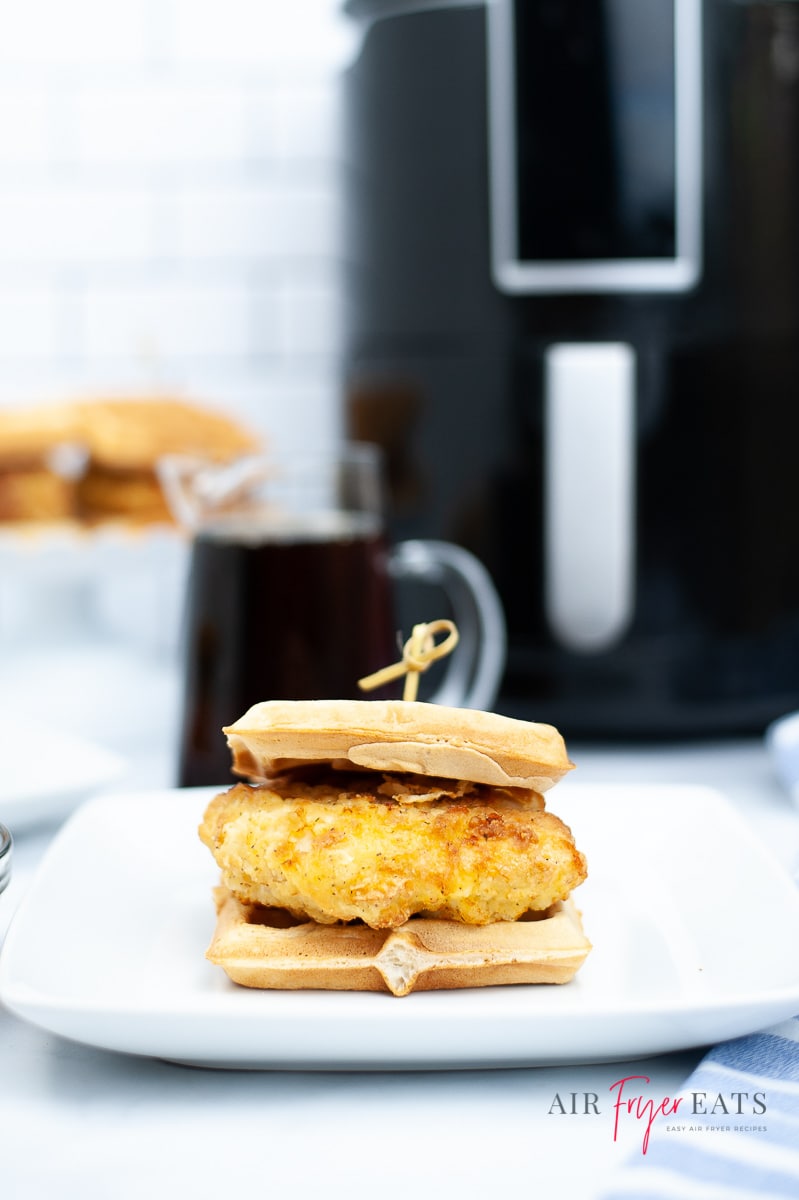 a chicken and waffles sandwich on a white plate in front of a black air fryer