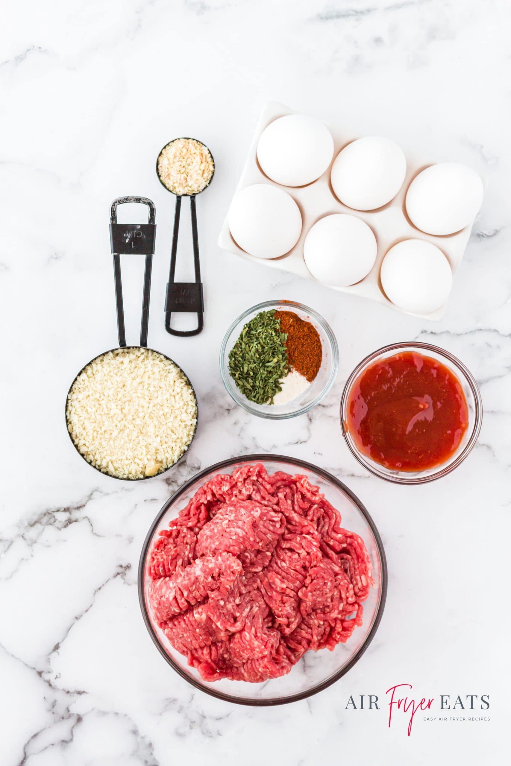 Ingredients for ninja foodi meatload laid out on a marble counter in separate dishes. There are eggs, ground beef, breadcrumbs, and seasonings.