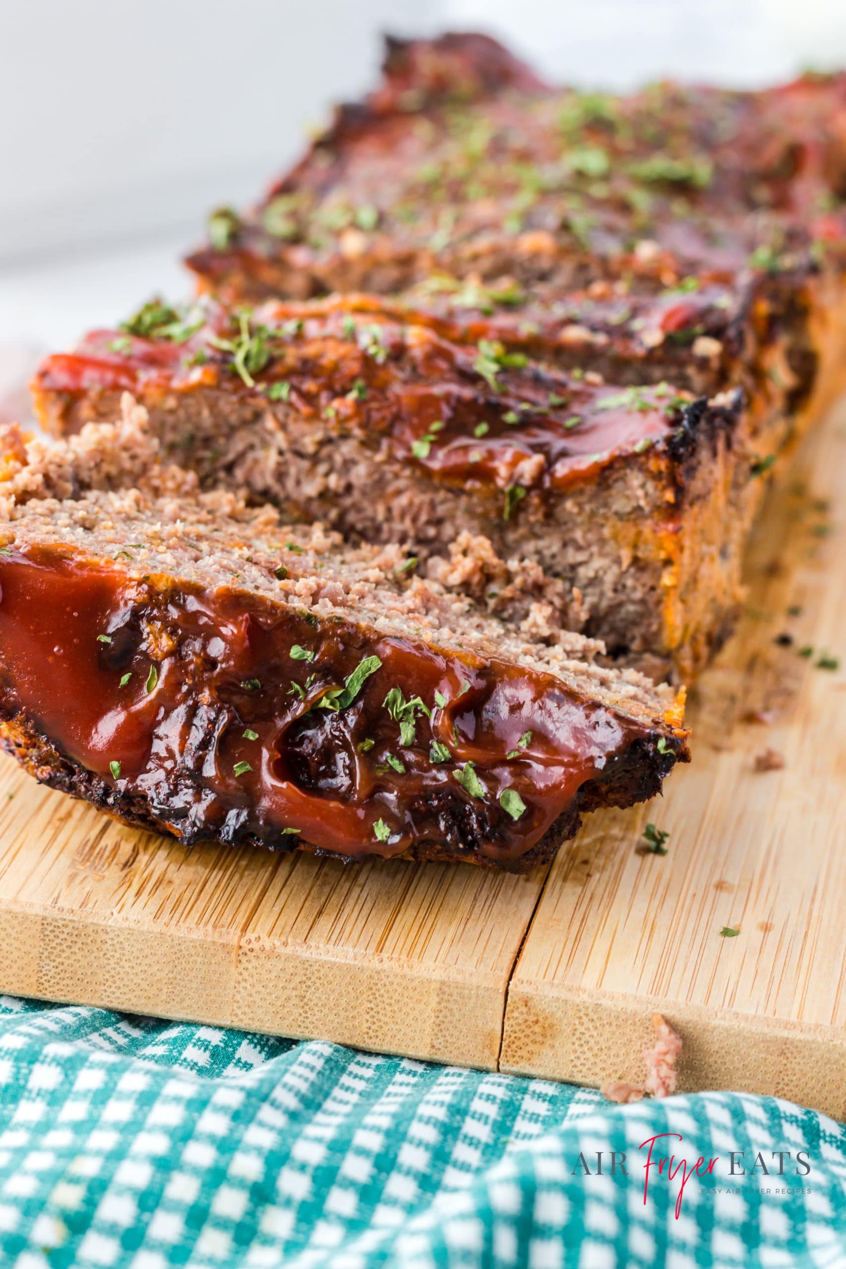 close up view of a meatloaf cooked in an air fryer with a crunchy top, sliced on a cutting board