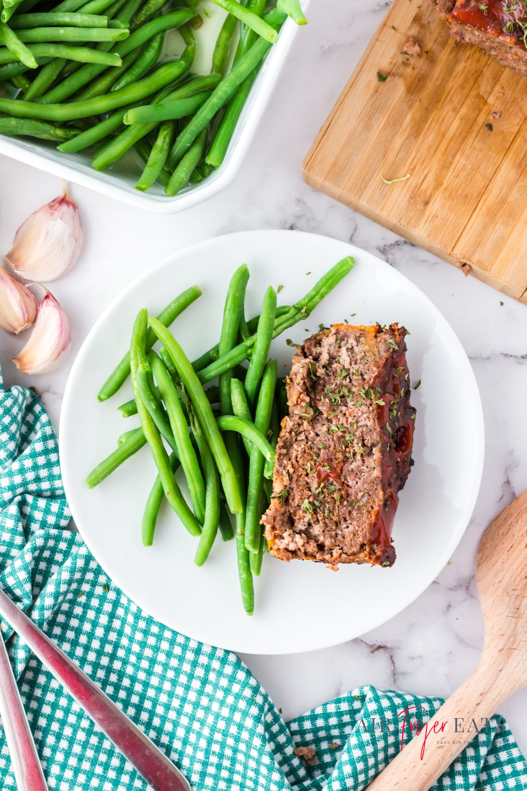 a round white plate with a slice of meatloaf and a side of green beans on a marble countertop