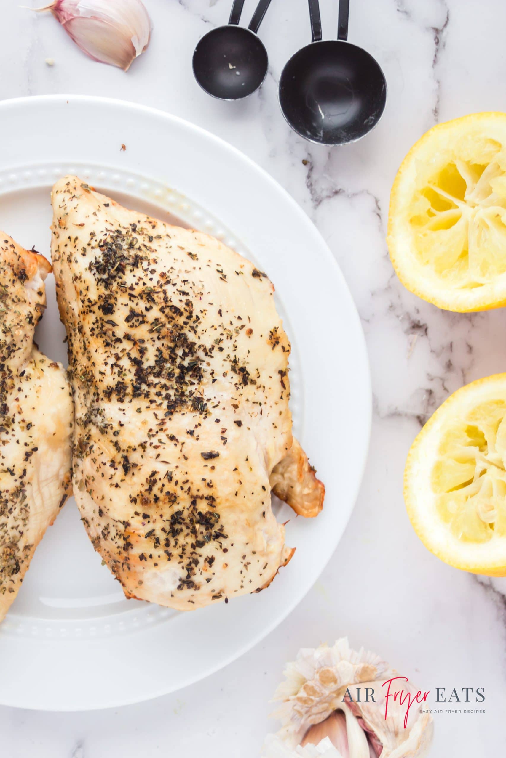 cooked chicken breast on a white plate next to two squeezed lemon halves.