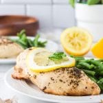 a seasoned chicken breast on a plate with a lemon slice on top.