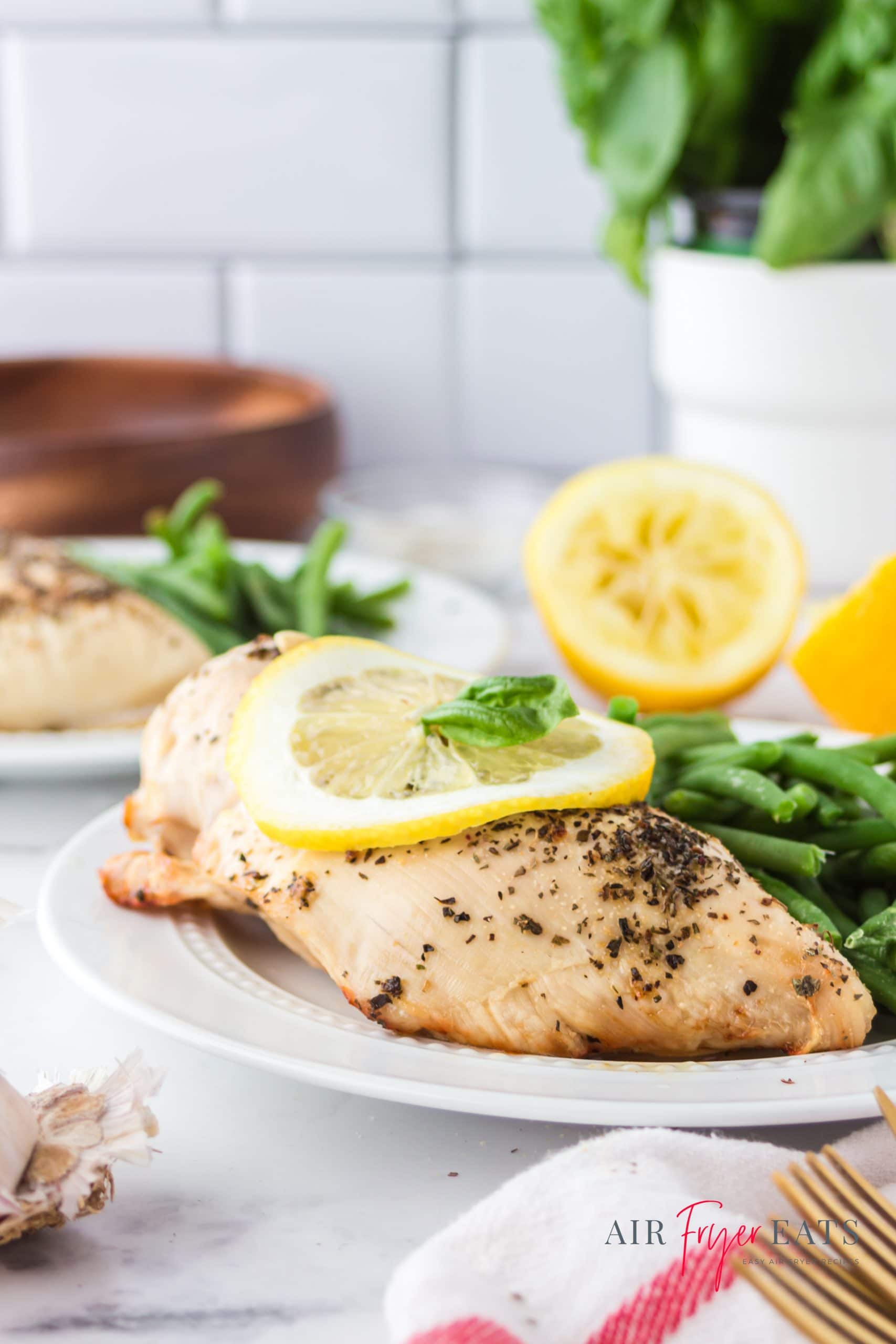 a seasoned chicken breast on a plate with a lemon slice on top.