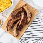 sliced BBQ ribs on a wooden cutting board next to a pan of macaroni and cheese