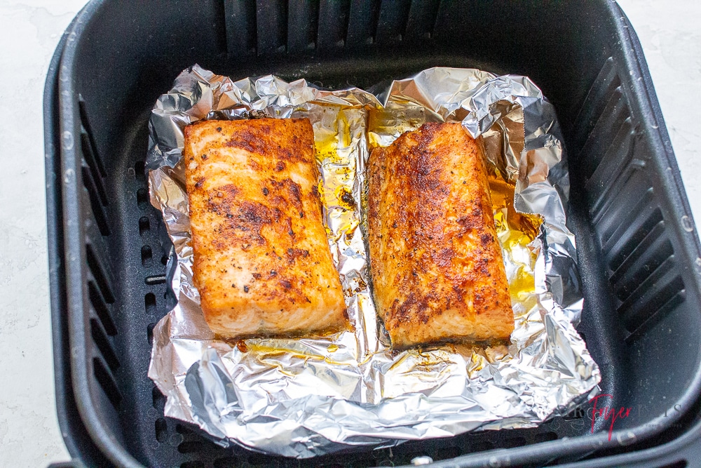 two pieces of cooked salmon on foil in air fryer in black air fryer basket