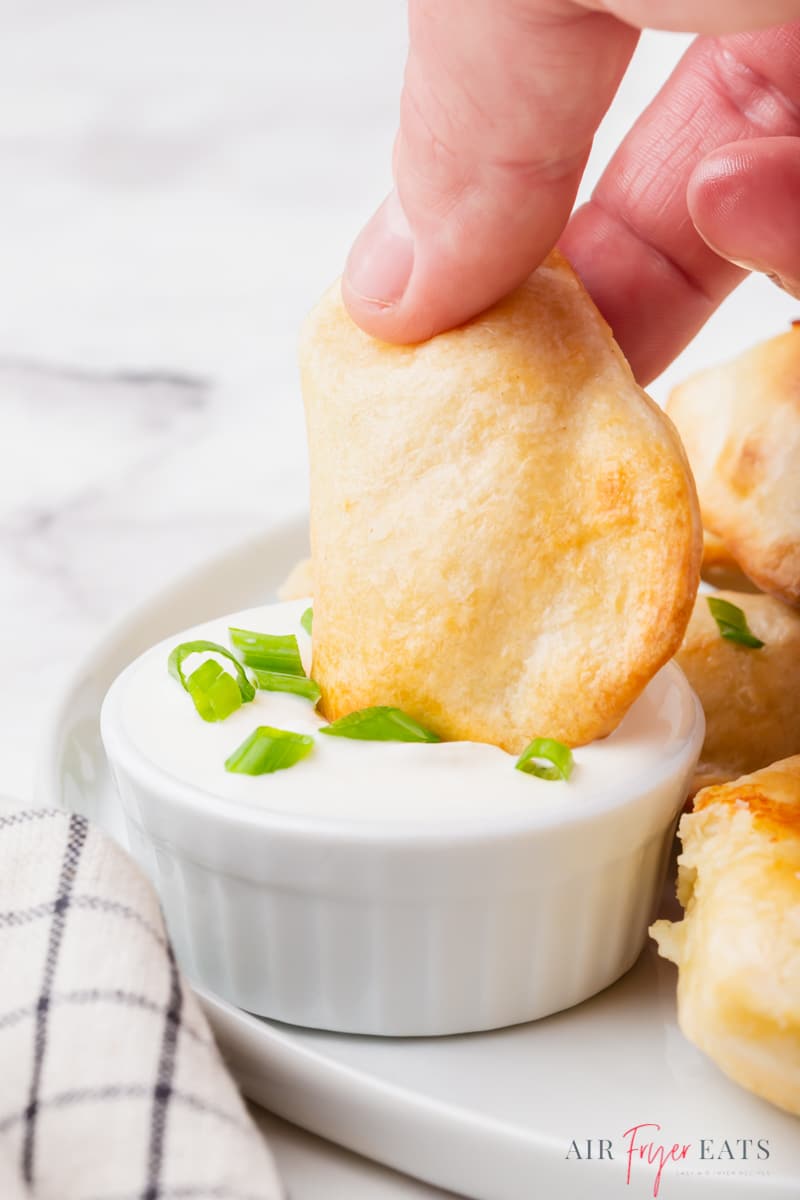 a hand dipping a pierogie into a creamy sauce.